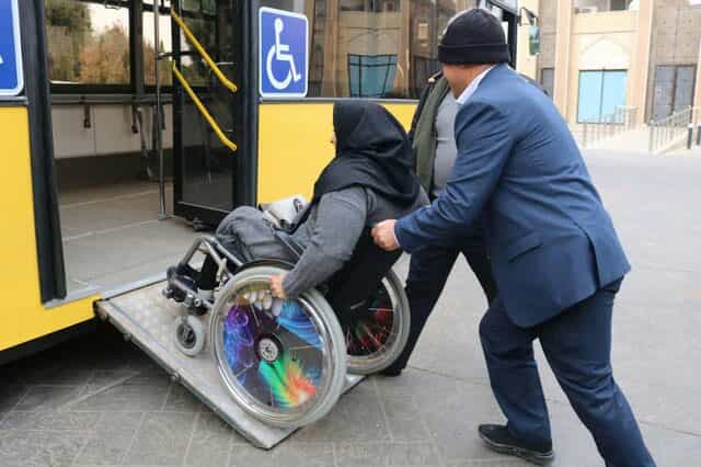 مردی یک زن را که روی فیلچر نشسته است وارد یک اتوبوس می‌کند.
