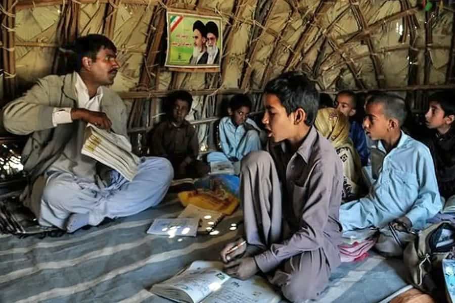 در یک چادر چند دانشآموز بلوچ روی زمین نشستهاند و یک معلم که او هم روی زمین نشسته است، به آنها درس میدهد. تصویری از خمینی و خامنهای نیز روی دیوارهی چادر دیده میشود.