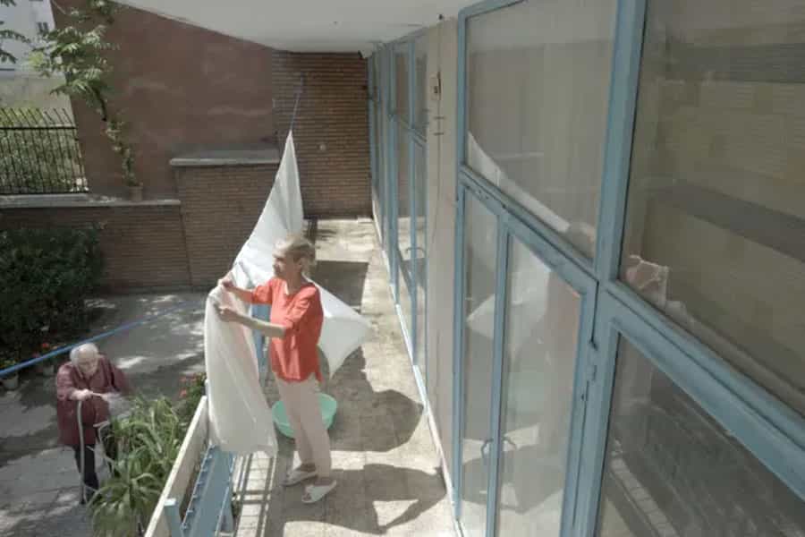 در تصویر حیاط خانه‌ای دیده می‌شود که در آن یک زن و مرد سالمند در حال کار هستند.