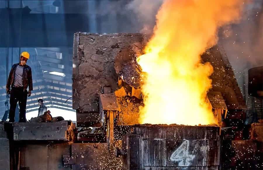 در تصویر یک کوره بزرگ ذوب آهن دیده میشود که در کنار آن کارگری ایستاده است.