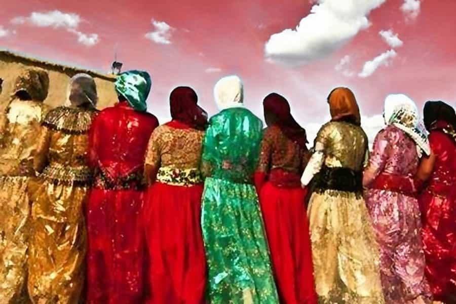 چند زن با لباس‌های کُردی دست در دست هم دارند. آن‌ها از پشت سر نشان داده شده‌اند و رنگ آسمان بالای سر آن‌ها قرمز است.