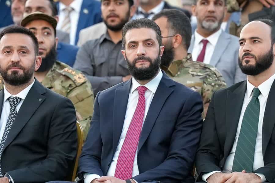 احمد الشرع، رئیس‌جمهور موقت سوریه در مراسمی در میان دو تن از مسئولان دولتی نشسته است.