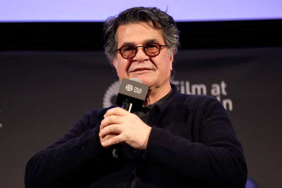 چهره جعفر پناهی با میکروفونی در دست در حال صحبت و با عینک دودی بر چشم.