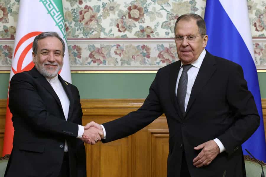 عباس عراقچی و سرگئی لاوروف در حالیکه میخندند دست یکدیگر را فشردهاند. پشت سر آنها پرچمهای ایران و روسیه دیده میشود.