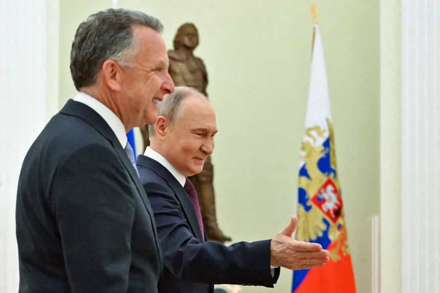 در تصویر ولادیمیر پوتین، رئیس جمهور روسیه از استیو ویتکوف، فرستاده ویژه ایالات متحده آمریکا، استقبال می‌کند. هر دو می‌خندند و در پسزمینه پرچ روسیه دیده می‌شود.