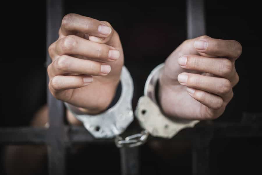 در تصویر دستهای دستبندزده یک زن پشت میلههای زندان دیده میشود.