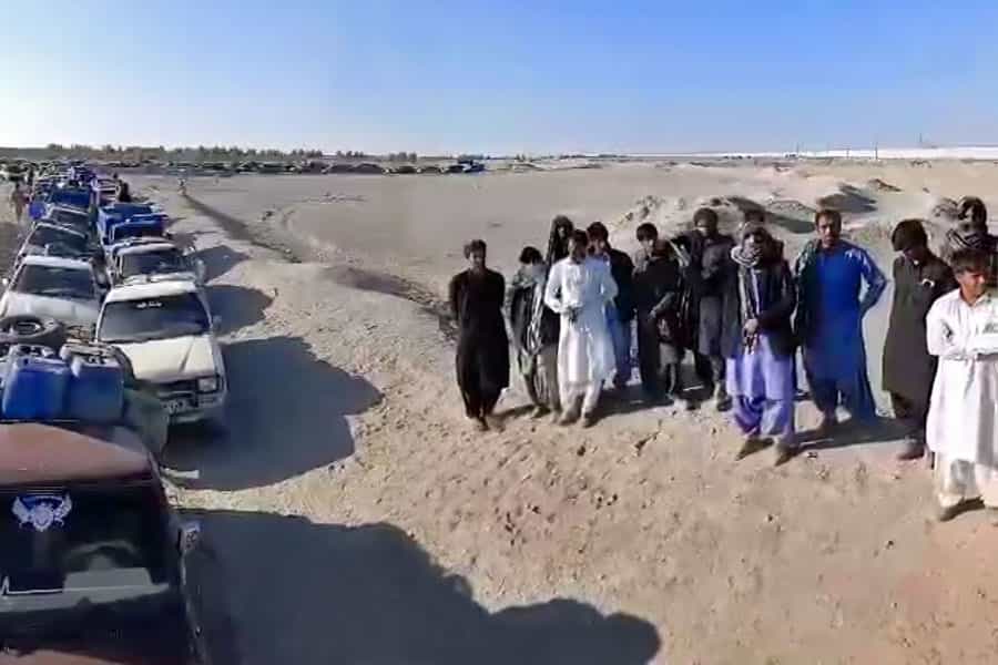 جمعی از سوختبران بلوچ در کنار خودروهای خود که در صفی طولانی قرار دارند، ایستادهاند.