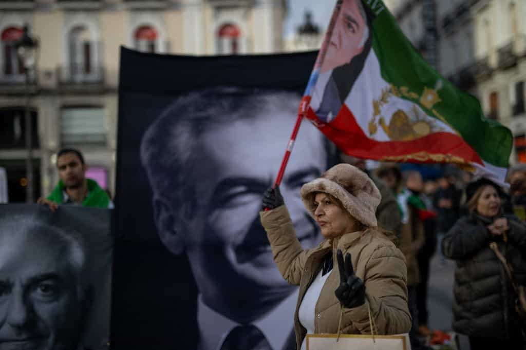 زنی که پرچم شیر و خورشید دست گرفته و عکس محمدرضا شاه پشت است در تظاهرات