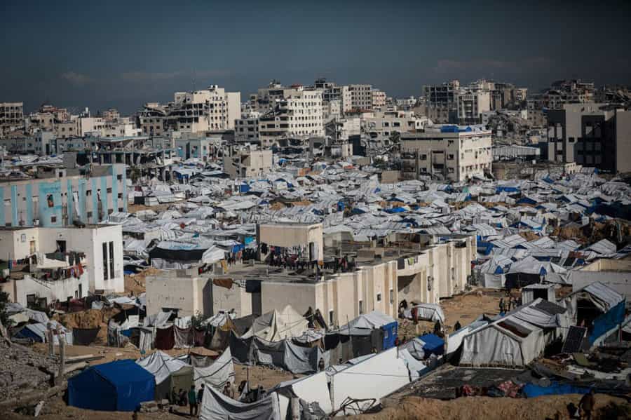 نمایی دور از شهر غزه که در آن چادرهایی در کنار ساختمان‌های ویران بنا شده‌اند و مردم آواره در آن‌ها زندگی می‌کنند.