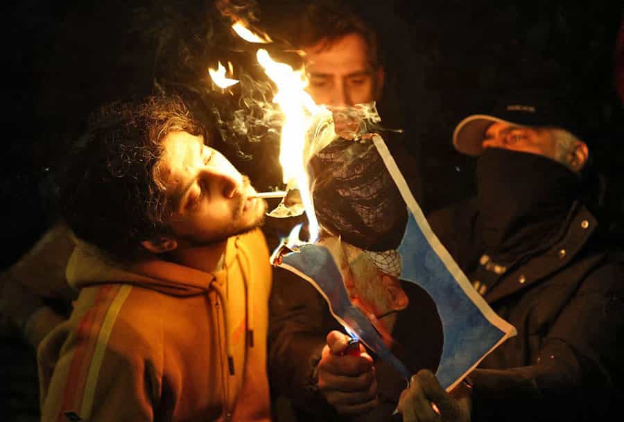 یک پسر جوان با آتش تصویر سوخته علی خامنه‌ای سیگاری روشن می‌کند.