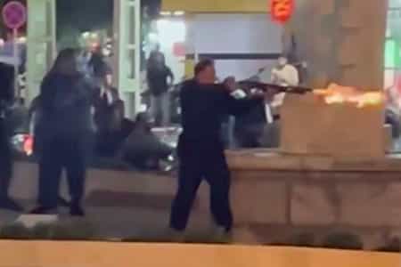 در خیابان هوا تاریک است و یکی از افراد امنیتی با تفنگ خود به سوی مردم معترض نشانه گرفته و شلیک کرده است.