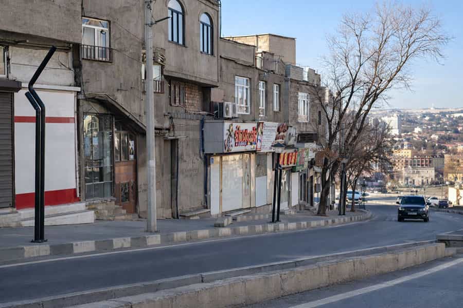 این تصویر یک خیابان سرازیری را نشان میدهد که تمامی مغازههای آن تعطیلاند و یک خودرو از آن عبور میکند.