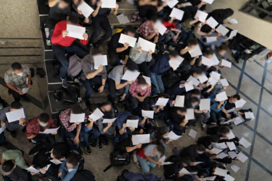 تصویری از بالا دانشجویان متحصن را نشان می‌دهد که روی پله‌های دانشگاه نشسته‌اند و برگه‌هایی در دست گرفته‌اند.