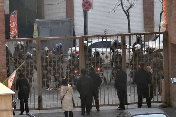 چندین مأمور امنیتی با کلاه‌خودها و موتورسیکلت‌های خود پشت نرده‌های در ورودی بیمارستان سینا تهران دیده می‌شوند. این سوی درِ نرده‌ای و در داخل محوطه بیمارستان عده‌ای به آن‌ها نگاه می‌کنند.