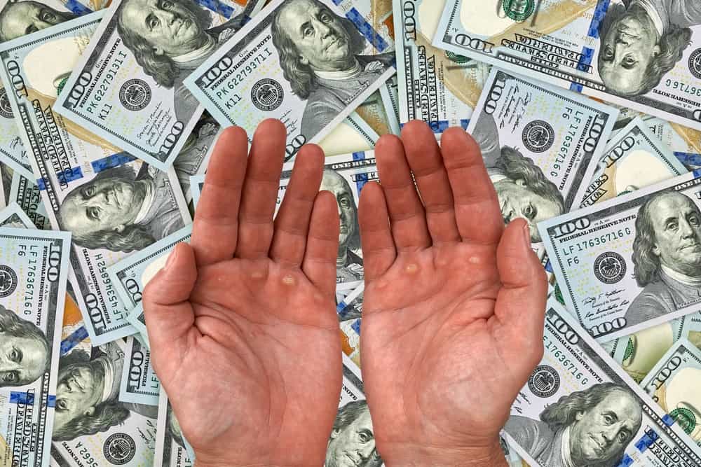 دو دست خالی باز شده‌اند و زیر آن‌ها انبوهی از اسکناس دلار دیده می‌شود.