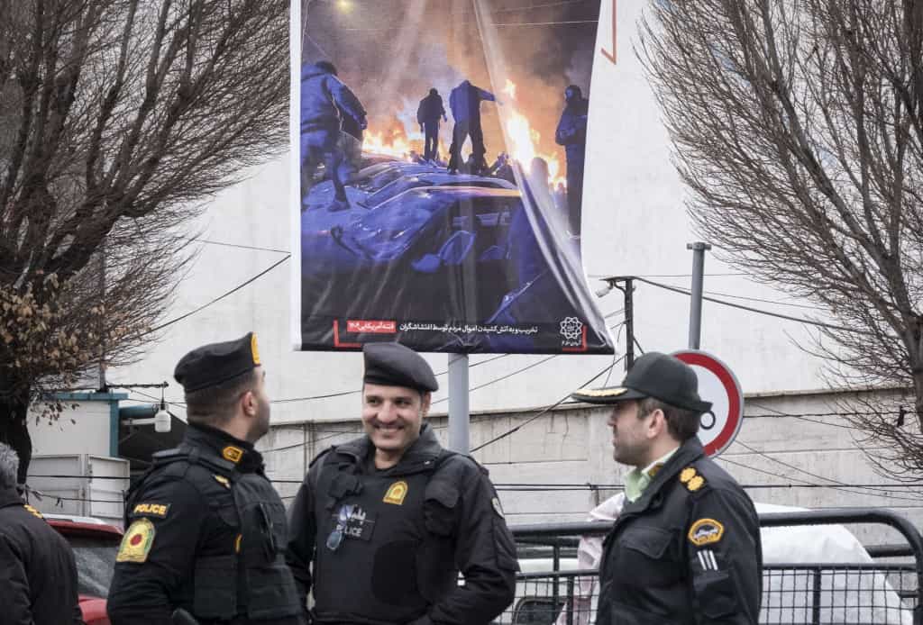 پلیس ایران در مرکز تهران، ایران، در تاریخ ۱۵ بهمن ۱۴۰۴، حدود یک ماه پس از اعتراضات مرگبار ضد دولتی در ایران، زیر یک بیلبورد که تصویری از ناآرامی‌ها در جریان یک جشنواره مذهبی دولتی به مناسبت سالگرد تولد امام مهدی را نشان می‌دهد، ایستاده‌اند.