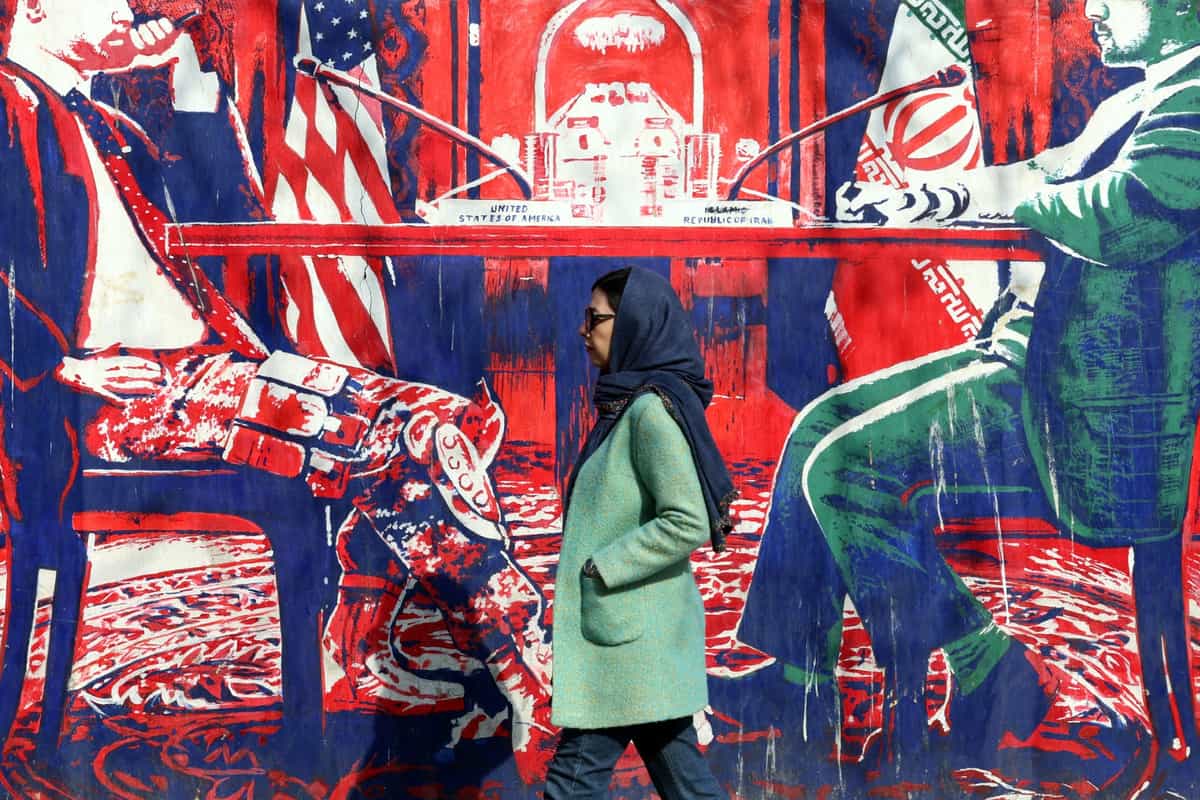 یک زن ایرانی در حال عبور از کنار نقاشی دیواری ضدآمریکایی است که میز مذاکره ایران و آمریکا را به تصویر می‌کشد. این نقاشی روی دیوارهای بیرونی سفارت سابق ایالات متحده در تهران در تاریخ ۱۷ بهمن ۱۴۰۴ (۶ فوریه ۲۰۲۶) کشیده شده است.