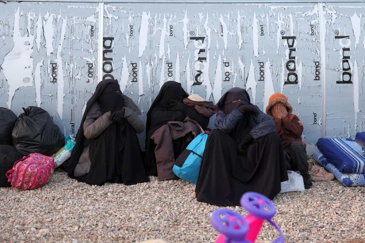 تصویر چند زن با چهره های پوشیده نشسته کنار یک دیوار