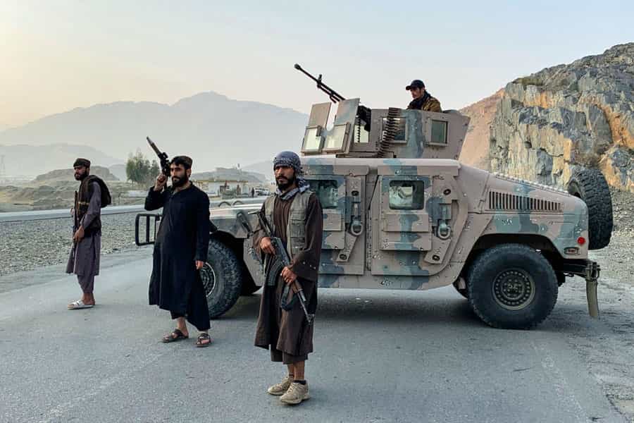 چند تن از نیروهای امنیتی طالبان در کنار یک خودرو نظامی، مسلح ایستاده‌اند.