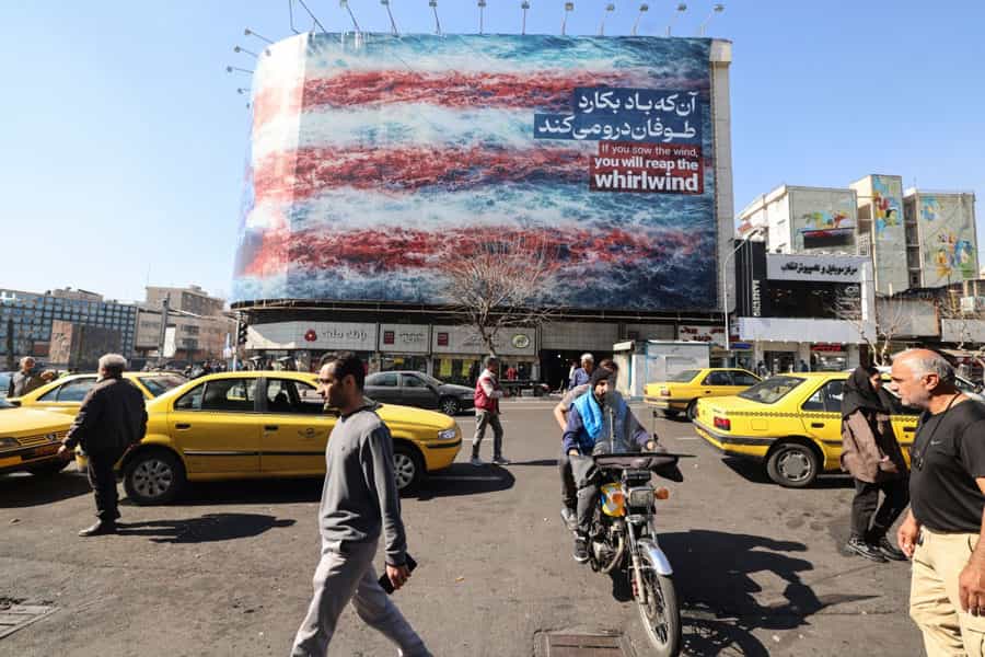 مردم در حال عبور از کنار یک بیلبورد ضد آمریکایی بر روی ساختمانی در میدان انقلاب تهران ـ روی بیلبورد با پرچ آمریکا نوشته شده: «آن که باد بکارد، طوفان درو میکند».