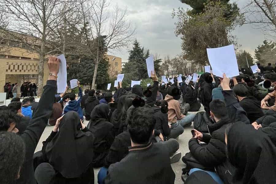 تصویری از دانشجویان دانشگاه مشهد که با برگههایی در دست روی زمین نشستهاند.