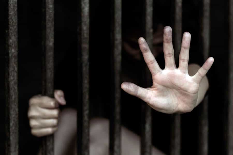 پشت میله‌های زندان یک کودک دیده می‌شود. او با یک دست میله زندان را گرفته و دست دیگر خود را از لای میله‌ها بیرون کشیده و باز کرده است.