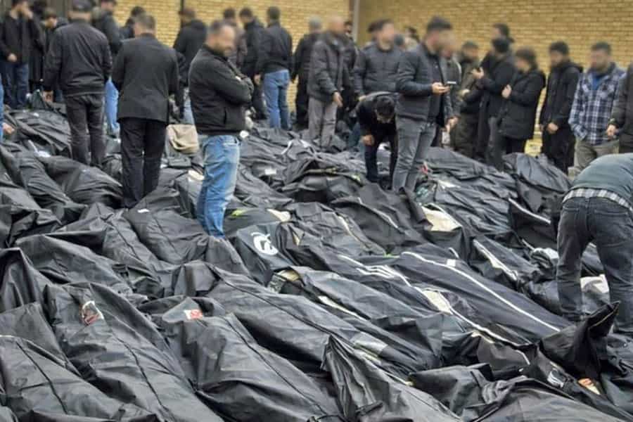 عده‌ای بالای پیکرهای کنار هم قرارگرفته‌ی جان‌باختگان کشتار اعتراضات ایستاده‌اند و در جست‌وجوی جسد عزیزان خود هستند.