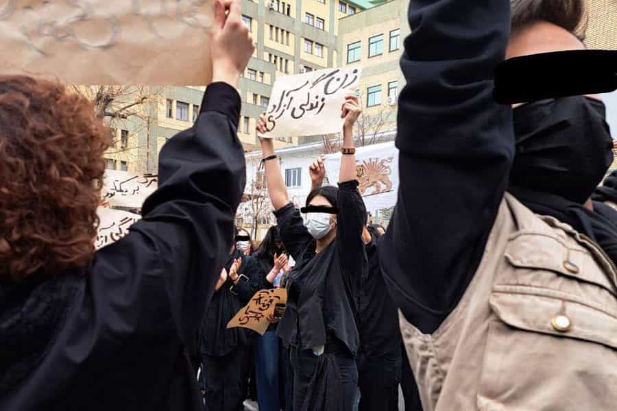 یک دانشجوی دختر در میان دیگر دانشجویان معترض پلاکارد «زن، زندگی، آزادی را در دست بلند کرده است.