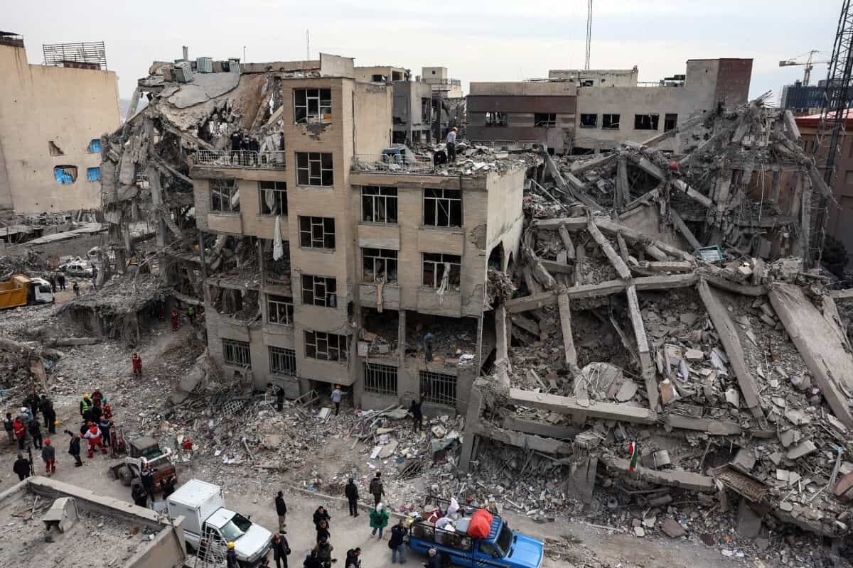 نیروهای امداد در بیرون یک ساختمان مسکونی آسیب‌دیده در تهران، در ۱۲ مارس ۲۰۲۶، جمع شده‌اند، در حالی که ساکنان در حال جمع‌آوری وسایل خود از زیر آوار هستند.