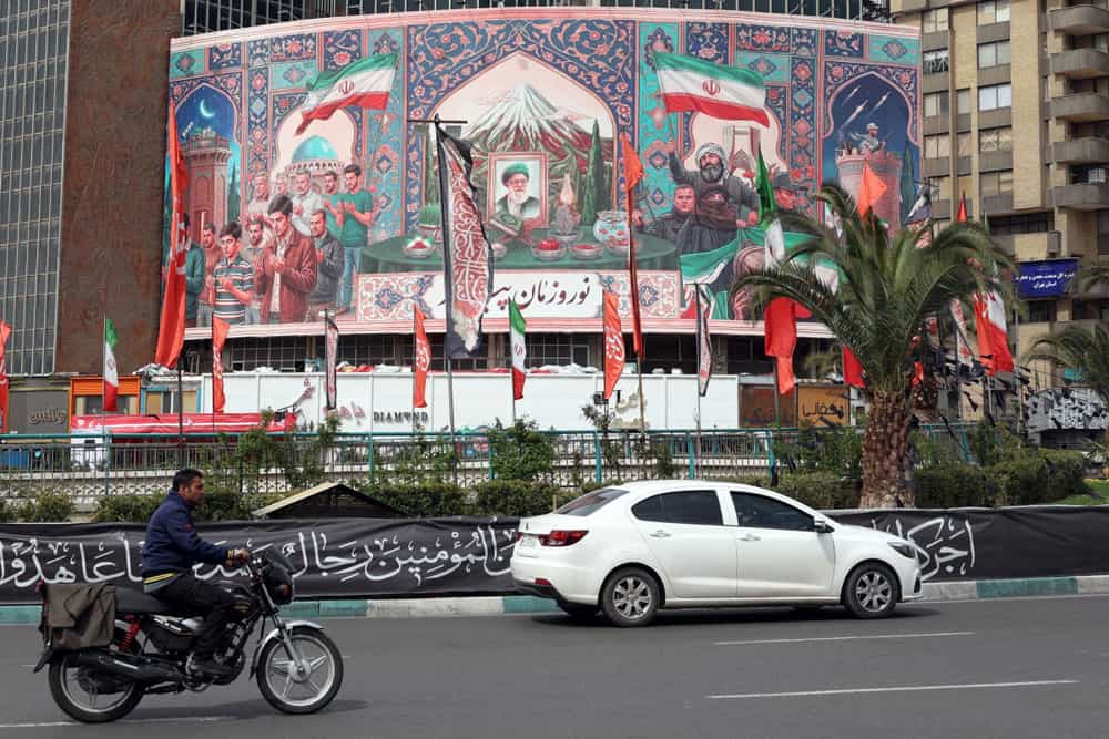 یک خودرو و یک موتورسیکلت در حال عبور از میدان ولیعصر تهران هستند. در پسزمینه تصویر یک بیلبورد بزرگ با تصویر علی خامنه‌ای قرار دارد که روی آن نوشته شده: «نوروزتان پیروز».