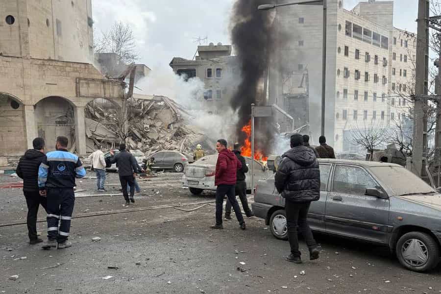 ساختمانی پس از حمله هوایی در میان آتش می‌سوزد و عده‌ای در خیابان به سوی محل حادثه می‌دوند.