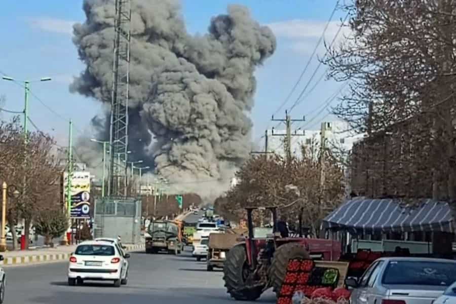 در انتهای یک بلوار، در دوردست، دود سیاه ناشی از یک انفجار شدید به آسمان برخاسته است. در بلوار چند خودرو در حال حرکتند و یک میوه فروش میوه‌های خود را در کنار بلوار قرار داده است.