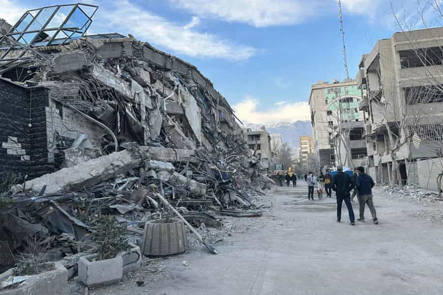 سمت چپ یک کوچه ویران شده است و چند نفر در کوچه دارند راه می روند.