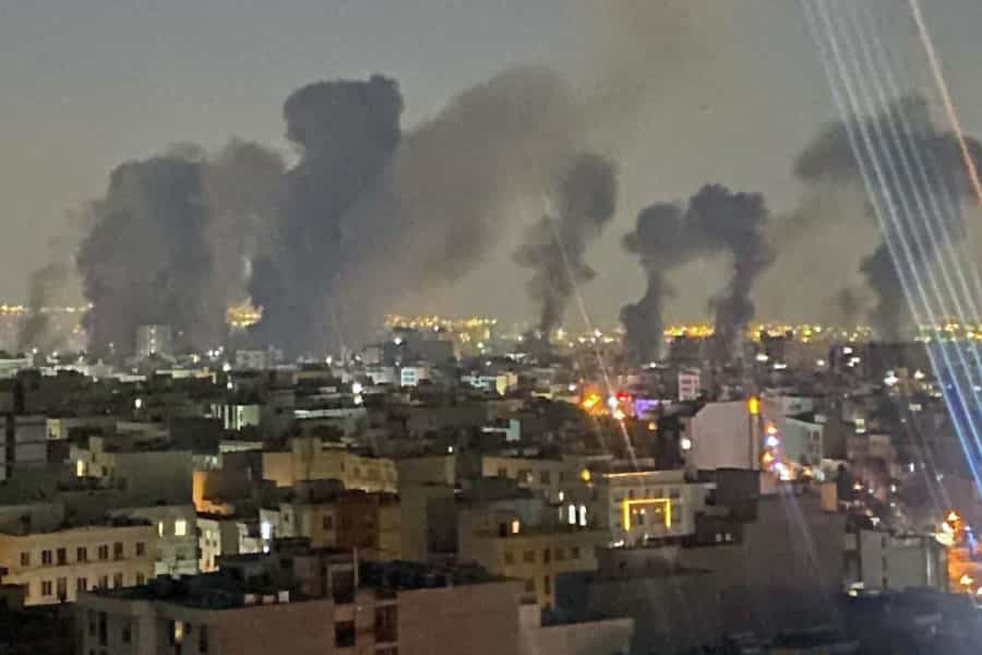 در تاریکی صبحگاهی تهران که هنوز چراغ‌ها روشن‌اند چندین بمب در انتهای تصویر منفجر شده‌اند.