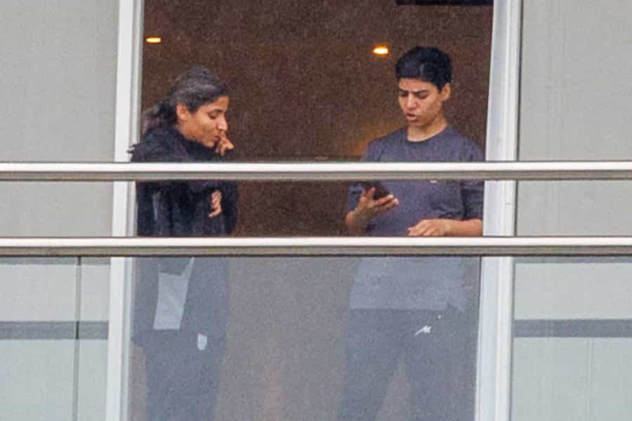 دو عضو تیم فوتبال زنان ایران بدون حجاب در بالکنی ایستاده‌اند و موبایل‌های خود را در دست دارند.