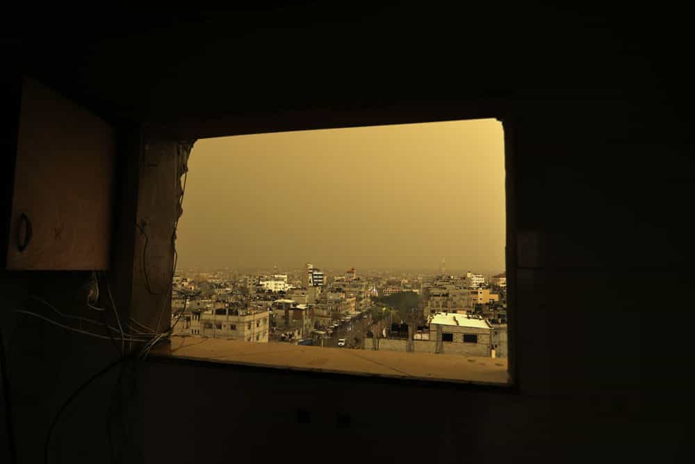 از دریچه‌ای بر روی یک دیوار ویران، شهری خاک‌گرفته دیده می‌شود.