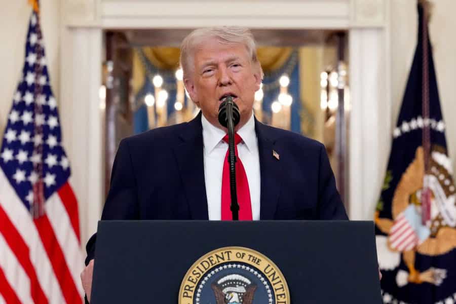 دونالد ترامپ پشت تریبون و میکروفون در حال سخنرانی است. پشت سر او پرچم آمریکا دیده می‌شود.