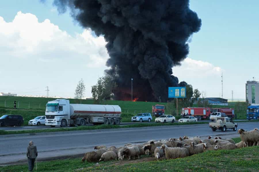 در یک جاده چندین خودرو و یک تانکر نفت در حال عبورند و چوپانی گله خود را در چمنزار کنار جاده چرا می‌دهد. بمبی در پس‌زمینه تصویر منجر شده و دود سیاهی به آسمان برخاسته است.