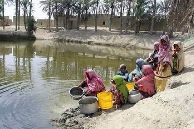 چند زن و کودک بلوچ در آب یک هوتگ ظرف میشویند.