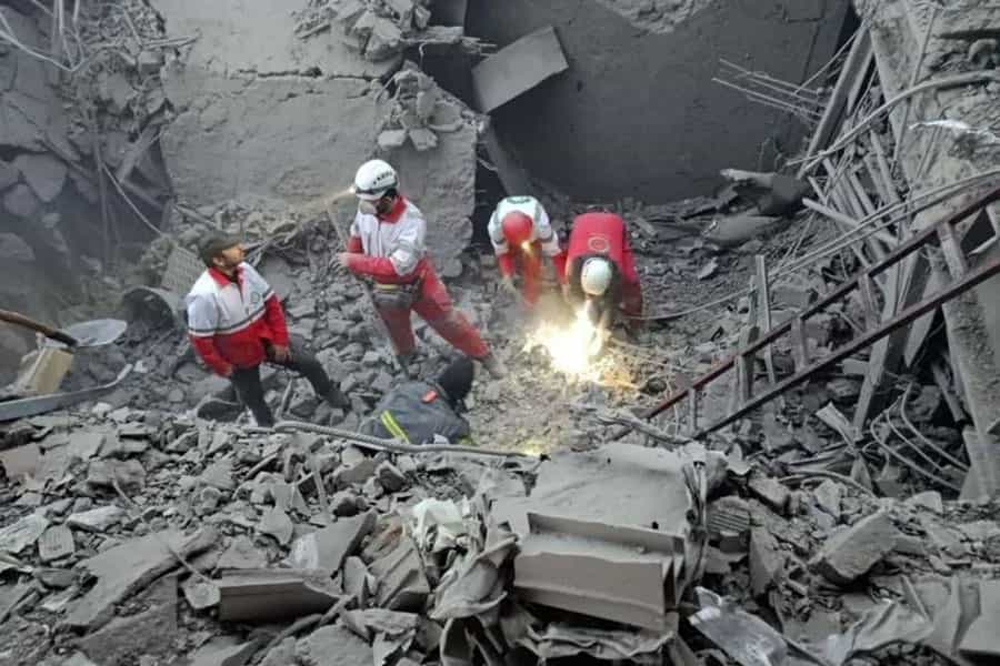 چند نیروی امدادگر در میان آوار پس از حمله هوایی در حال کار هستند.
