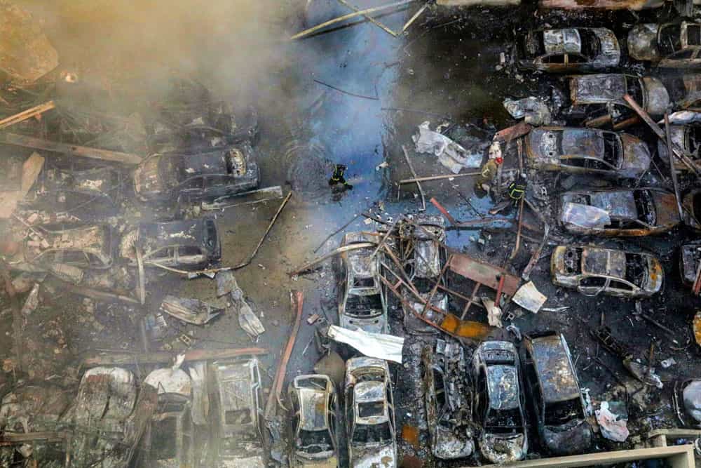 تصویری از بالا یک آتشنشان را نشان میدهد که از کنار خودروهای سوخته و متلاشیشده عبور میکند.