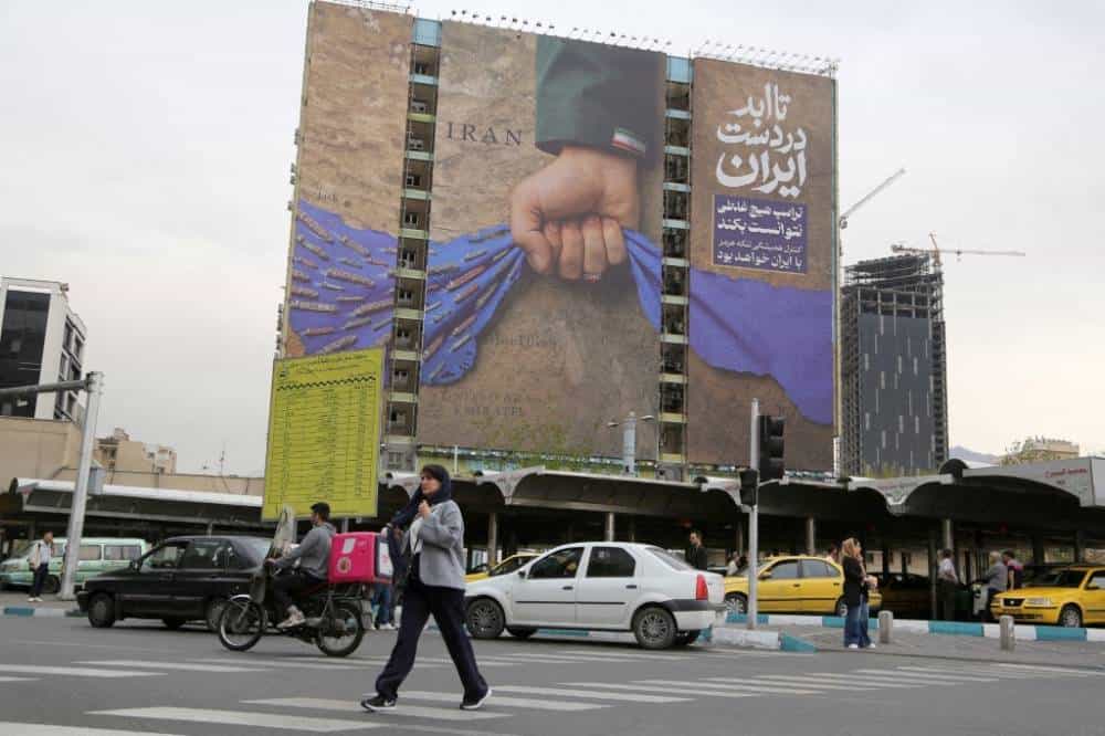 تصویری از یک بیلبورد بزرگ درباره بستن تنگه هرمز در میدان ونک تهران. مردم و خودروها در خیابان دیده می‌شوند.