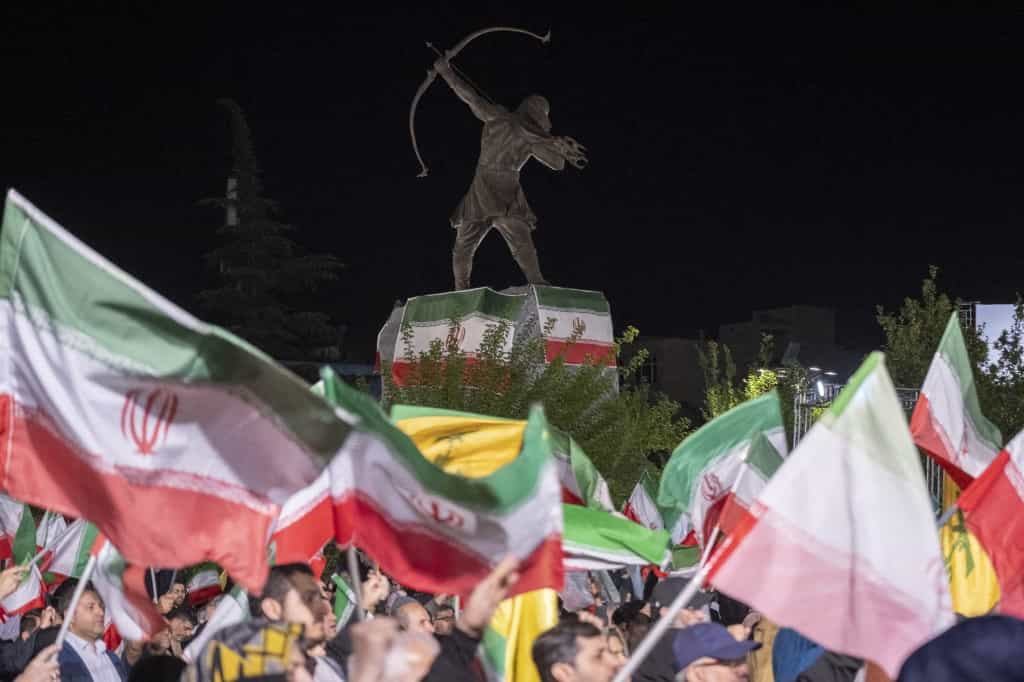طرفداران دولت در ۲۵ آوریل ۲۰۲۶ در شمال تهران، ایران، در حال تکان دادن پرچم‌های ملی در زیر مجسمه آرش کمانگیر هستند.