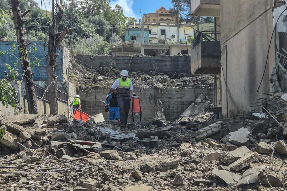 امدادگران لبنانی با برانکاردهایی در دست، در میان آوارهای ناشی از بمباران اسرائیل در حال جست‌وجو هستند.