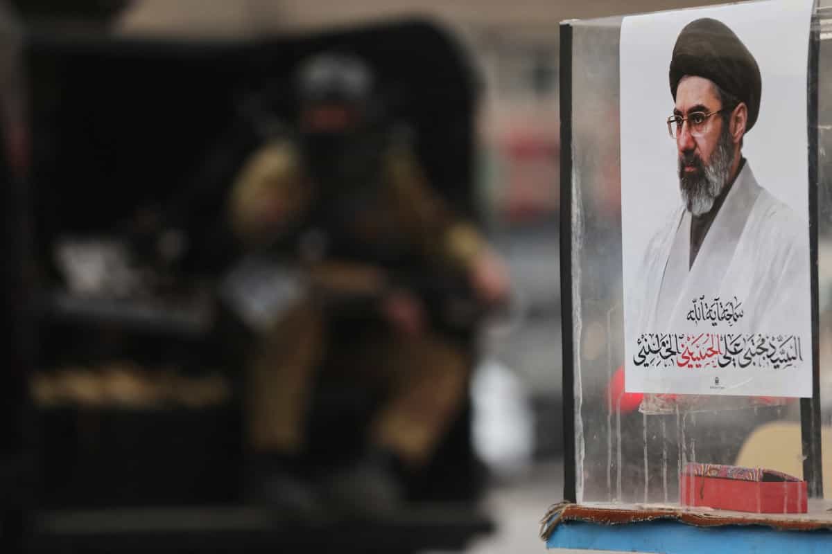 «یک نیروی حشدالشعبی در حال نگهبانی در کنار پرترهٔ مجتبی خامنه‌ای، رهبر معظم ایران، طی یک تجمع طرفدار ایران در میدان التحریر بغداد در دوم آوریل ۲۰۲۶. سفارت آمریکا در بغداد روز دوم آوریل هشدار داد که گروه‌های مسلح مورد حمایت ایران در عراق ممکن است طی یک یا دو روز آینده به شهر حمله کنند. عراق اکنون به درگیری میان آمریکا، اسرائیل و ایران کشیده شده و حملات متعددی هم علیه منافع آمریکایی و هم علیه گروه‌های طرفدار ایران در این کشور انجام شده است.»