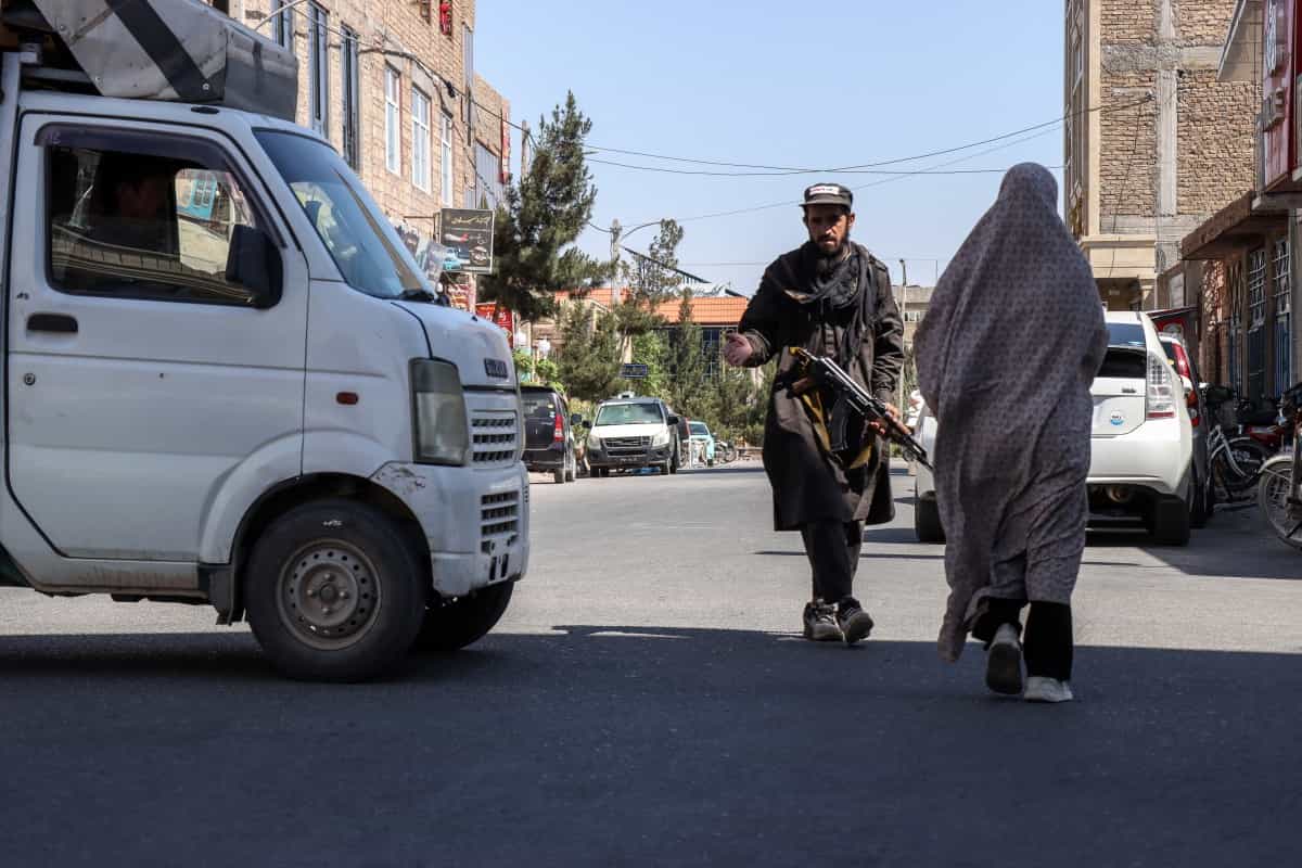 یک زن برقعپوش افغان در ۱۱ ژوئن ۲۰۲۶ از کنار یک نیروی امنیتی طالبان که در بیرون مسجدی در شهرک المهدی، شهرستان جبرئیل استان هرات نگهبانی میداد، عبور میکند.