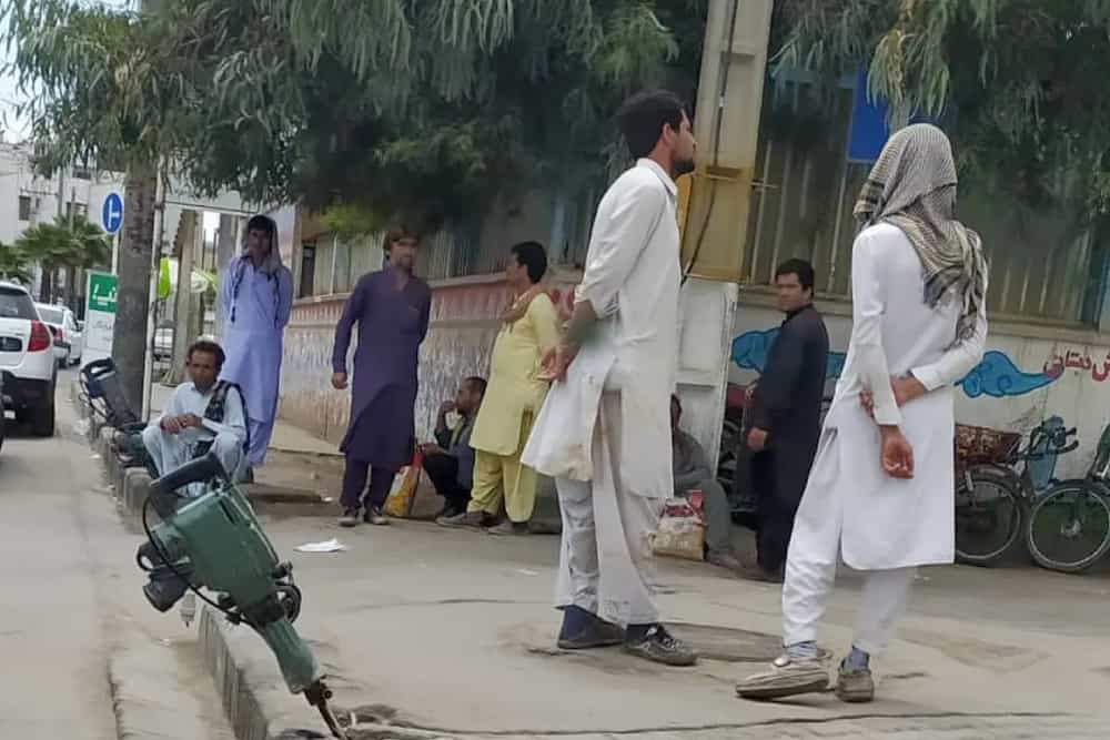 چند کارگر بلوچ با لباس بلوچی در خیابان ایستاده اند.