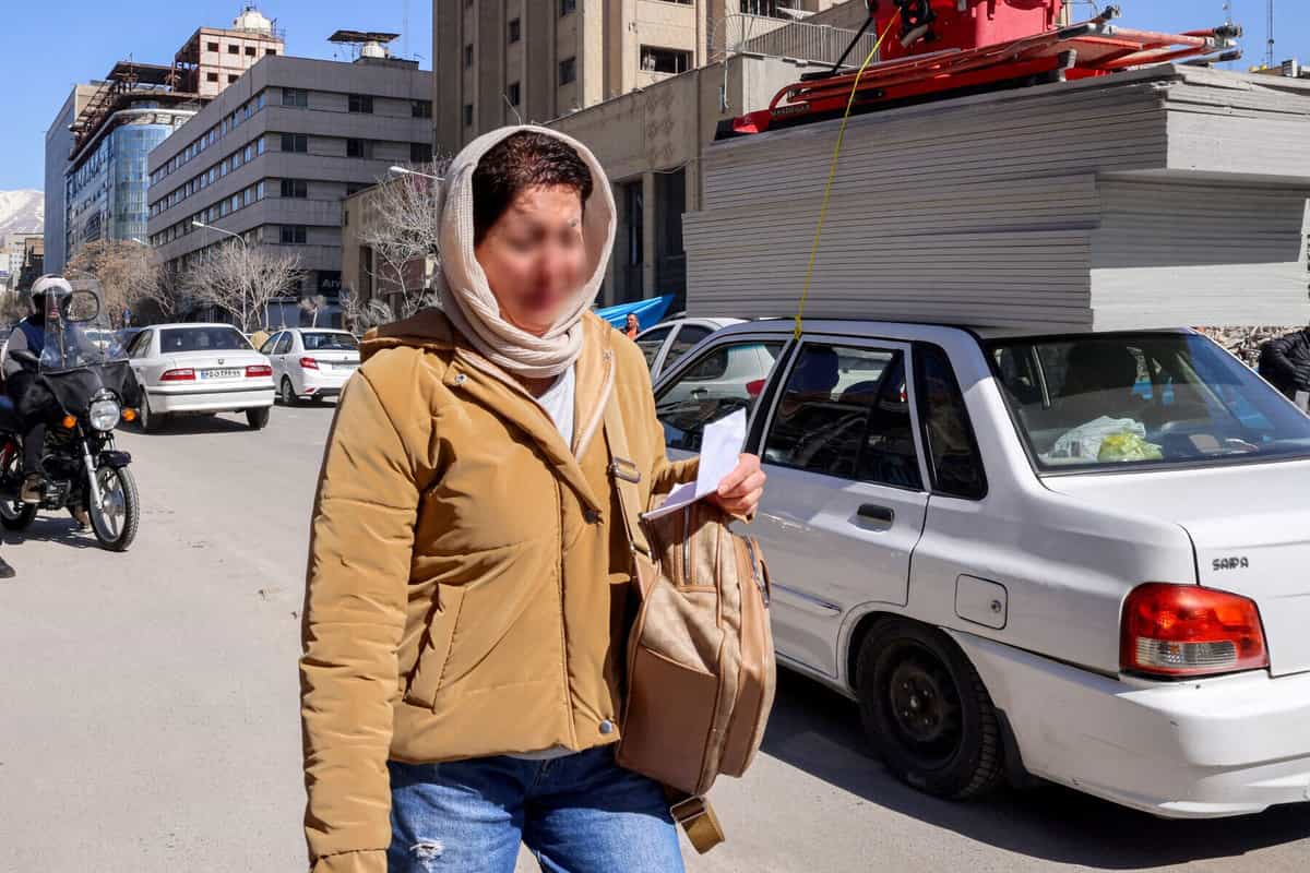 زنی در حال عبور از کنار ساختمانهای فروریخته و آسیبدیده در نزدیکی میدان فردوسی تهران در ۳ مارس ۲۰۲۶ واکنش نشان میدهد