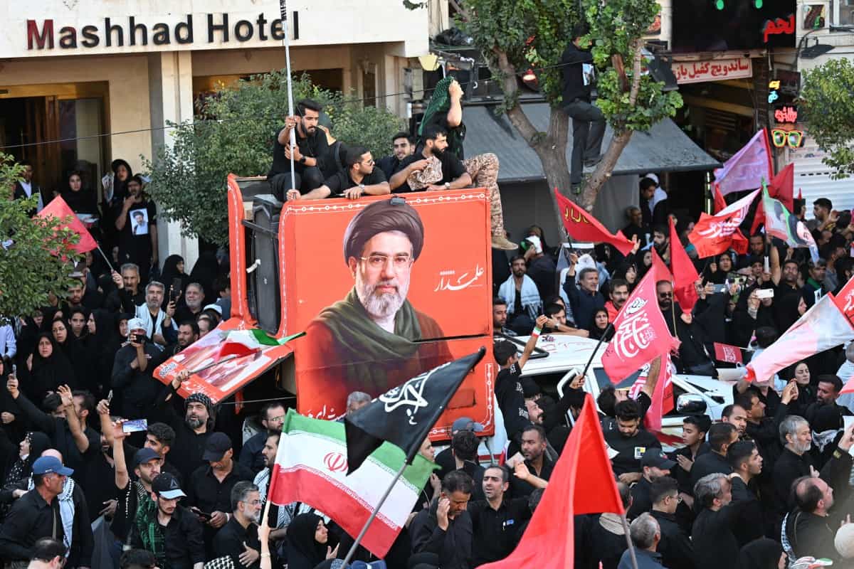 جمعیت عزاداران در خیابانی در اطراف تصویری از مجتبی خامنهای، رهبر ایران، پیش از تشییع جنازه علی خامنهای، رهبر مقتول ایران و اعضای خانوادهاش، پیش از دفن او در حرم امام رضا