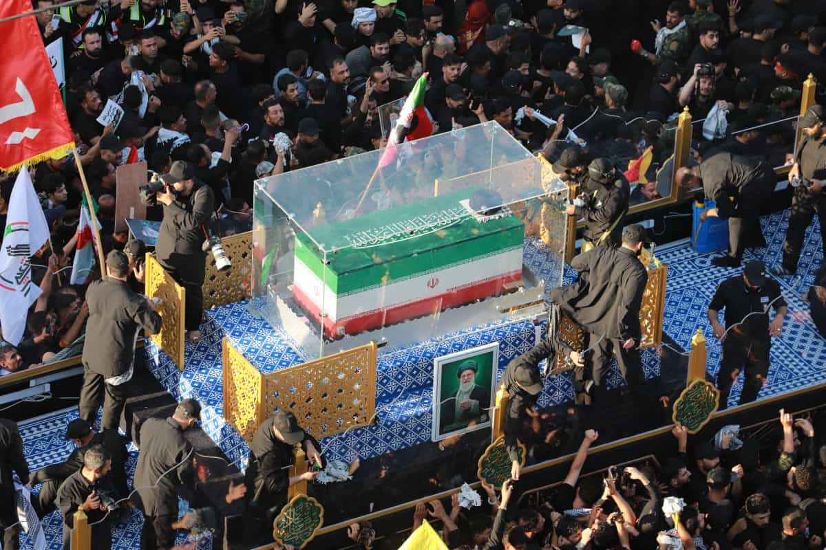 تابوت علی خامنهای در محفظه شیشهای در میان جمعیت دیده میشود. دور تابوت پرچم جمهوری اسلامی پیچیده شده است.